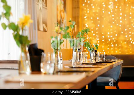 An elegant evening reception table set with candles, glassware, and fresh flowers against a twinkling fairy light backdrop Stock Photo