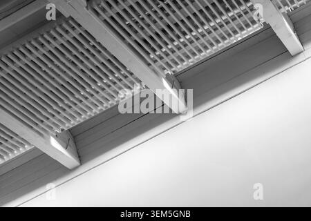 Minimal black and white photograph of a white interior ceiling featuring exposed wooden beams and louvered lattice panels, emphasizing architectural l Stock Photo