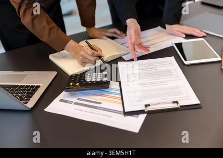 Business professionals collaborating at a modern office table, analyzing financial reports, using a laptop, calculator, and tablet to review data and strategize for future growth Stock Photo