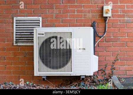 External air conditioning condenser unit installed beside a brick building wall as part of a commercial HVAC system Stock Photo