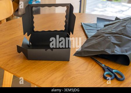 Open black cardboard box with transparent window near crumpled tissue paper on a wooden table. Concept: e-commerce packaging Stock Photo