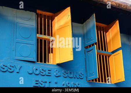 A low angle view of vibrant yellow wooden window shutters open against a bright blue wall on a heritage building in Kochi, Kerala, India Stock Photo