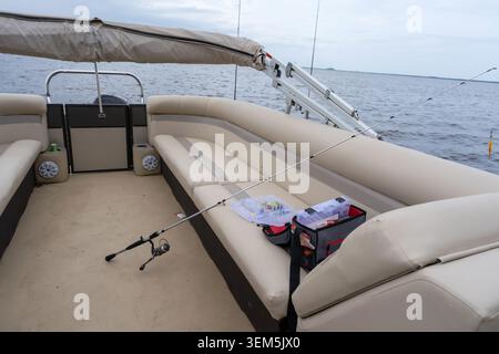 A high-quality horizontal lifestyle photograph showing a modern fishing rod and spinning reel laid out on the beige leather seat of a pontoon boat. Ne Stock Photo