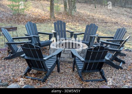 A high-angle horizontal photograph showing an empty circular seating area with black Adirondack chairs surrounding a stone brick fire pit. Located on Stock Photo