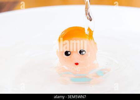 Water pouring over a small rubber baby toy with air bubbles. Small plastic doll being washed under a stream of clean water, bath time concept. Stock Photo