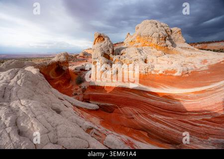 View of the unique White Pocket sandstone formations with swirling red layers and white textures under dramatic storm clouds in Coconino County, Arizo Stock Photo