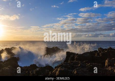 Atlantic waves breaking against volcanic rocks with sea spray illuminated by warm evening sunlight in Tenerife, Spain. Stock Photo
