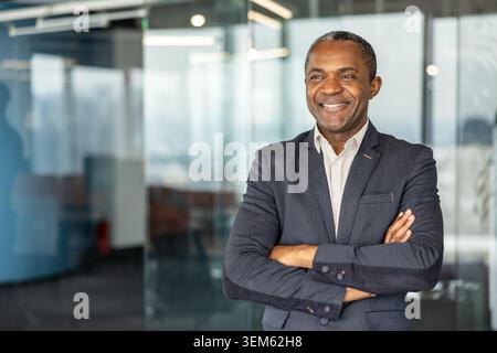 Confident professional businessman standing with folded arms in a modern corporate office, looking away and smiling, representing leadership, success, and executive excellence Stock Photo