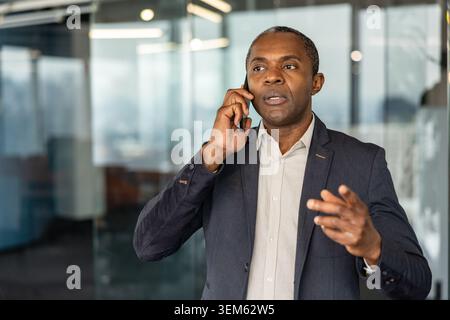 Professional businessman having an important conversation on his mobile phone, communicating with a client or colleague while standing in a contemporary office environment Stock Photo