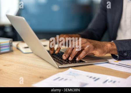 Businessman hands typing on a laptop amid reports and charts on a wooden desk, focused on digital communication, productivity and remote professional work and analysis Stock Photo