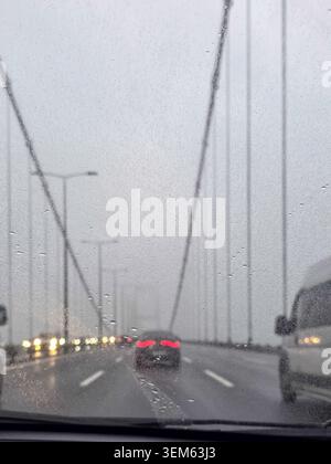 View of cars driving across a suspension bridge through a rainy windshield with wet asphalt and overcast sky in Besiktas, Istanbul, Turkey. Stock Photo