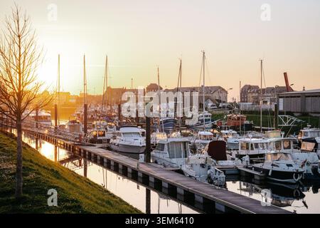 Numerous motorboats and sailboats moored along the floating docks in the harbor of Le Treport, France. The warm light of the setting sun reflects on t Stock Photo