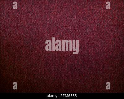 Dark red carpet texture background. Close-up of burgundy fabric, rug, or upholstery material with a woven pattern and subtle dark vignette edges. Stock Photo