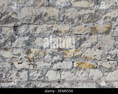 Rough weathered old stone wall texture background with irregular grey, white, and yellow stones and visible mortar. Stock Photo