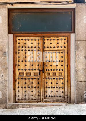 European rustic antique wooden double door with decorative iron studs and small pedestrian wicket door set in a stone wall facade. Stock Photo