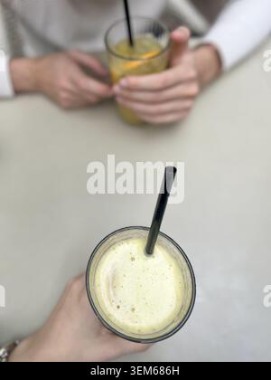 View of two people holding glasses of fresh fruit juice with black straws on a light-colored table Beylikduzu, Istanbul, Turkiye. Stock Photo