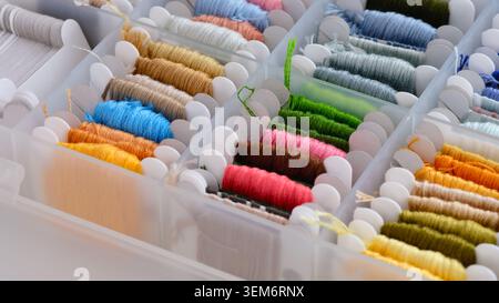 A plastic organizer box filled with colorful embroidery floss wound onto white plastic bobbins. Close-up Stock Photo
