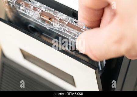 Close up of hand inserting transparent audio cassette tape into vintage deck player. Retro analog music culture concept Stock Photo
