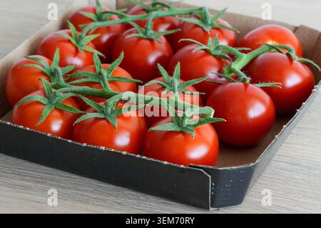 Cherry tomatoes in a cardboard box on a wooden table, top view. Tomatoes from the store. Stock Photo