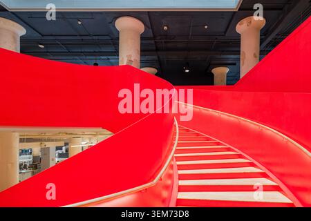 Memphis, United States, MAY 24, 2026 - A bright red curved staircase with wooden treads winds through a modern industrial interior featuring exposed Stock Photo