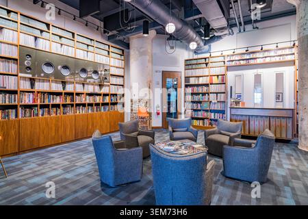 Memphis, United States, MAY 24, 2026 - A contemporary reading room featuring floor-to-ceiling wooden bookshelves, blue upholstered armchairs, and Stock Photo