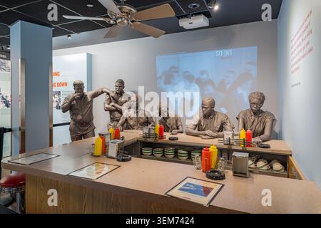 Memphis, United States, MAY 24, 2026 - Bronze statues of African American students sitting at a diner counter in a museum exhibit with a projected Stock Photo