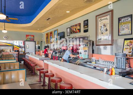 Memphis, United States, MAY 25, 2026 - Two employees working behind a long counter in a vintage-style diner featuring a blue ceiling, red bar stools, Stock Photo