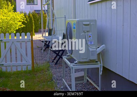 Turku, Finland - June 2th 2026 - A Midea brand outdoor air source heat pump unit is mounted on a metal stand next to the wooden wall of a residential Stock Photo