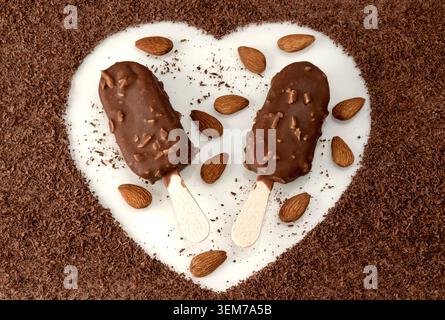 A heart-shaped arrangement of chocolate almond ice cream on a stick, whole nuts, and grated chocolate. Romantic sweets. Close-up top view. Stock Photo