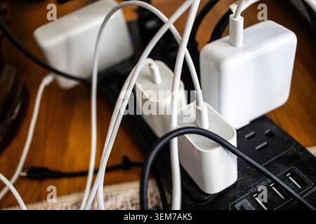 USB-C chargers plugged into a power strip or surge protector, charging electronic devices with tangled cords, closeup of charging bricks Stock Photo