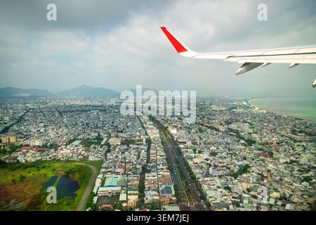 Plane takes off over city of Da Nang in Vietnam, aerial view from inside of cabin porthole at city Stock Photo