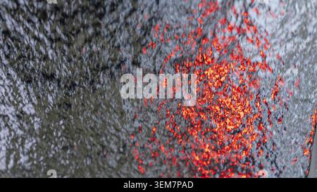 Textured surface displays vibrant red and orange reflections against a dark background, creating a striking visual contrast and dynamic appearance Stock Photo