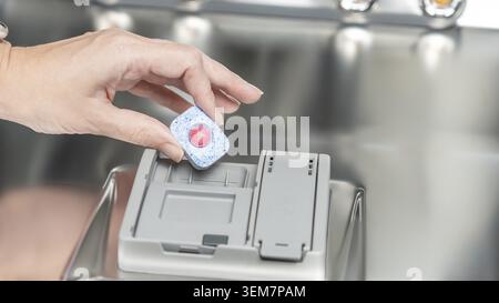 Hand is inserting a dishwasher tablet into the compartment of a stainless steel dishwasher, highlighting modern kitchen appliance features and usabili Stock Photo