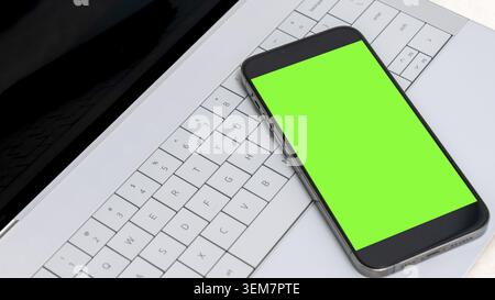 Smartphone mock up featuring a vibrant green screen, positioned on a stylish laptop keyboard, ideal for showcasing digital design concepts and creativ Stock Photo