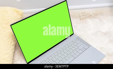 Laptop mock up featuring a vibrant green screen placed on a soft fur rug, ideal for showcasing digital content and creative design projects Stock Photo