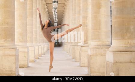 A female ballet dancer performs a perfect arabesque en pointe in a sunlit colonnade, where classical architecture meets expressive movement Stock Photo