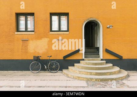 Black bicycle near orange-yellow wall of the old residential building in Copenhagen, Denmark Stock Photo