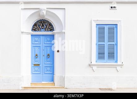 Facade of an old Maltese residential building with a blue wooden door and a window with closed shutters Stock Photo