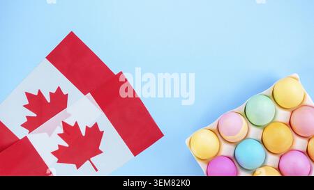Colorful Easter eggs pack and two canadian flags on blue background with space for text. Spring flat lay. Pastel painted eggs in box Stock Photo