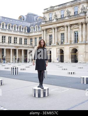 Young fashionable woman standing on striped column of Palais Royal art installation in Paris, France. Urban lifestyle and travel concept Stock Photo