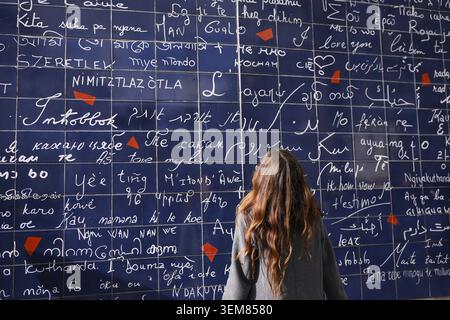 Young woman stands in front of the famous I Love You Wall in Paris, reading love messages written in many different languages Stock Photo