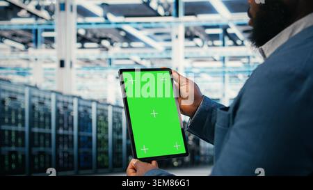 Green screen mockup tablet in server room used by worker to enhance hardware operational effectiveness. Data center engineer using chroma key isolated screen device to monitor gear, camera A close up Stock Photo