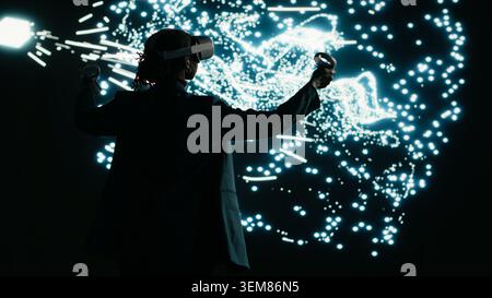 Programmer optimizes AI neural network data flow using virtual reality simulation, adjusting nodes. Computer scientist uses VR headset gear to manipulate artificial intelligence architecture, camera B Stock Photo