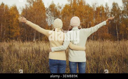 Back view of happy cheerful young two women friends in autumn park enjoying warm weather, joyful girlfriends together standing outdoors, wearing sweat Stock Photo