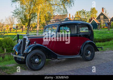 Vintage oldtimer car parked in front of traditional green Dutch house during golden hour Stock Photo