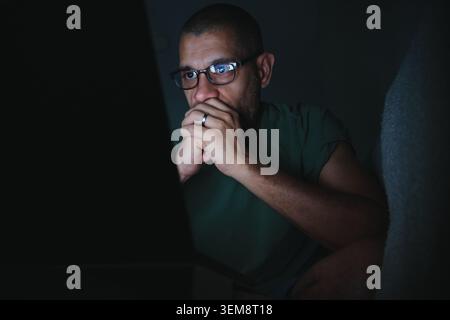 Man with glasses focusing on his laptop screen at night Stock Photo