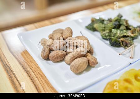 Unshelled peanuts rest on a white plate in a Korean dining setting. This close-up beautifully captures the authentic charm of natural, unprocessed ing Stock Photo