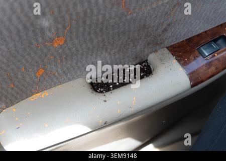A close view inside a vehicle showing a gray fabric seat with a ripped seam, exposing dark material beneath. Surrounding area features orange rust-lik Stock Photo