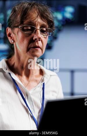Senior IT programmer in data center working on laptop, setting up high bandwidth dedicated multiplayer gaming servers to accommodate more traffic from worldwide locations and avoid disruptive lag Stock Photo