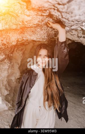 Woman cave portrait young female explorer posing inside a rocky cave with black jacket and white hoodie in warm light Stock Photo